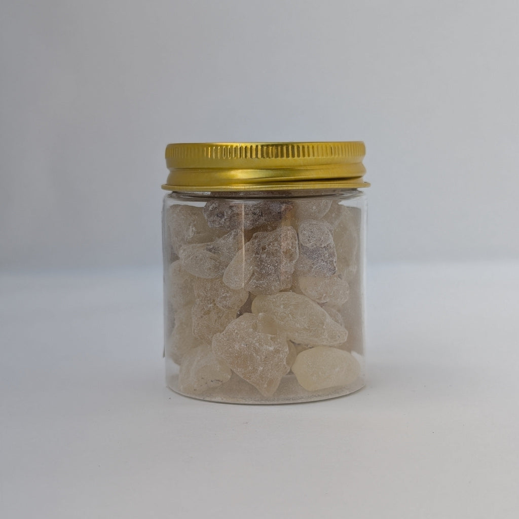 A small clear plastic jar filled with rough, translucent incense gum tears, sealed with a metallic gold screw-top lid, set against a plain light grey background.